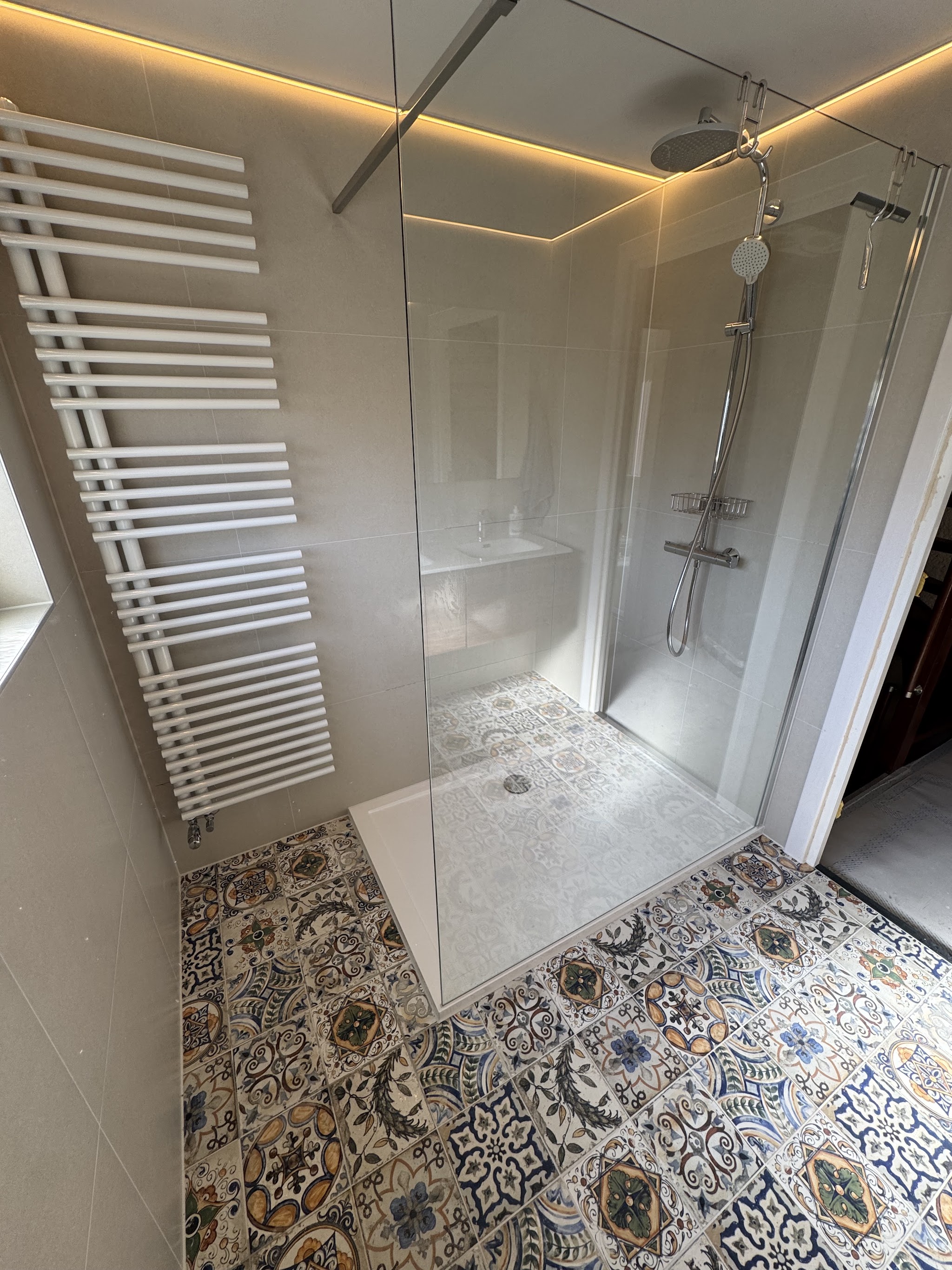 Inloopdouche met glazen wand, regendouche, witte handdoekradiator en patroontegels op de vloer