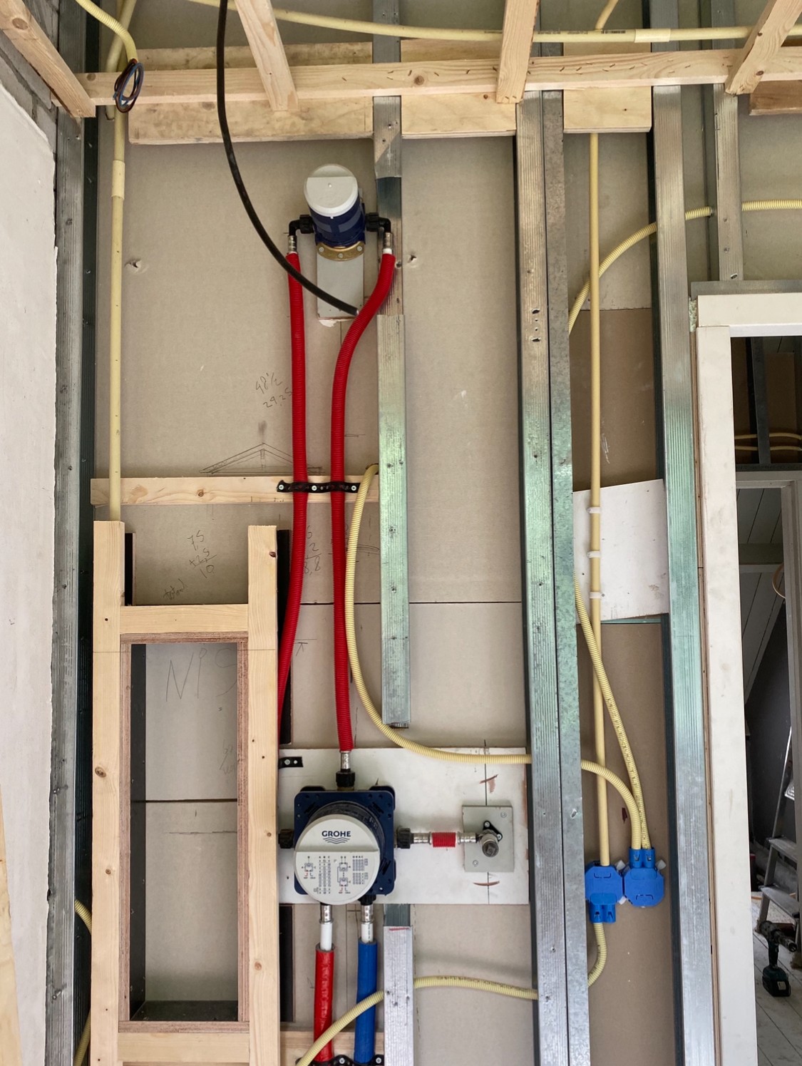 Open wand met watermeter, rode en blauwe waterleidingen en een verdeler tussen metalen profielen